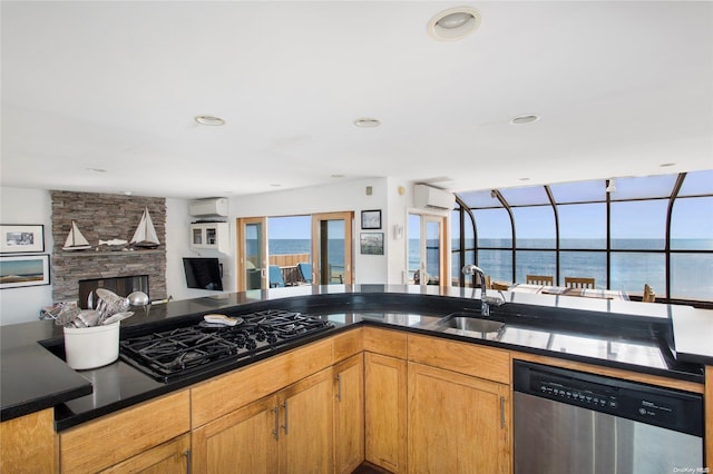 kitchen featuring stainless steel dishwasher, black gas stovetop, a wall mounted AC, a water view, and a stone fireplace