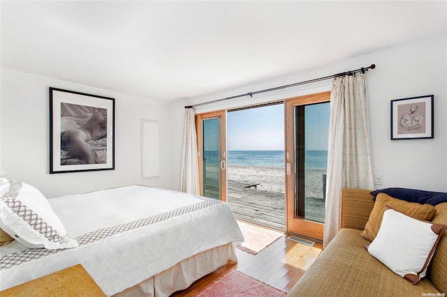 bedroom featuring access to exterior, a view of the beach, a water view, and light hardwood / wood-style flooring