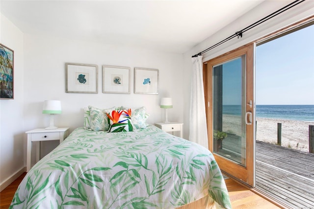 bedroom featuring a view of the beach, access to outside, light wood-type flooring, and a water view