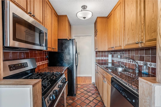 kitchen with dark stone counters, sink, dark tile patterned floors, appliances with stainless steel finishes, and tasteful backsplash