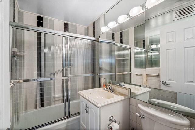 full bathroom with vanity, toilet, bath / shower combo with glass door, and tile walls