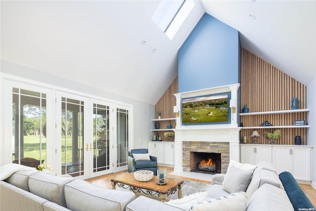 living room with a skylight, a stone fireplace, high vaulted ceiling, and light hardwood / wood-style floors