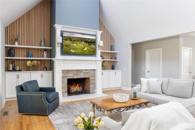 living room with high vaulted ceiling, light hardwood / wood-style floors, and a stone fireplace