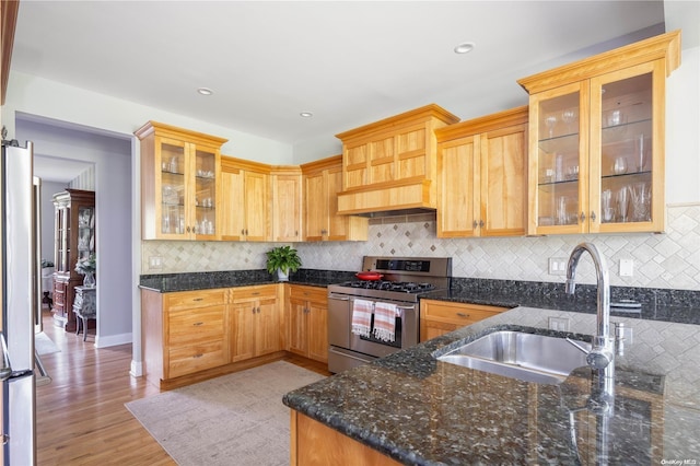 kitchen with decorative backsplash, appliances with stainless steel finishes, light wood-type flooring, sink, and dark stone countertops