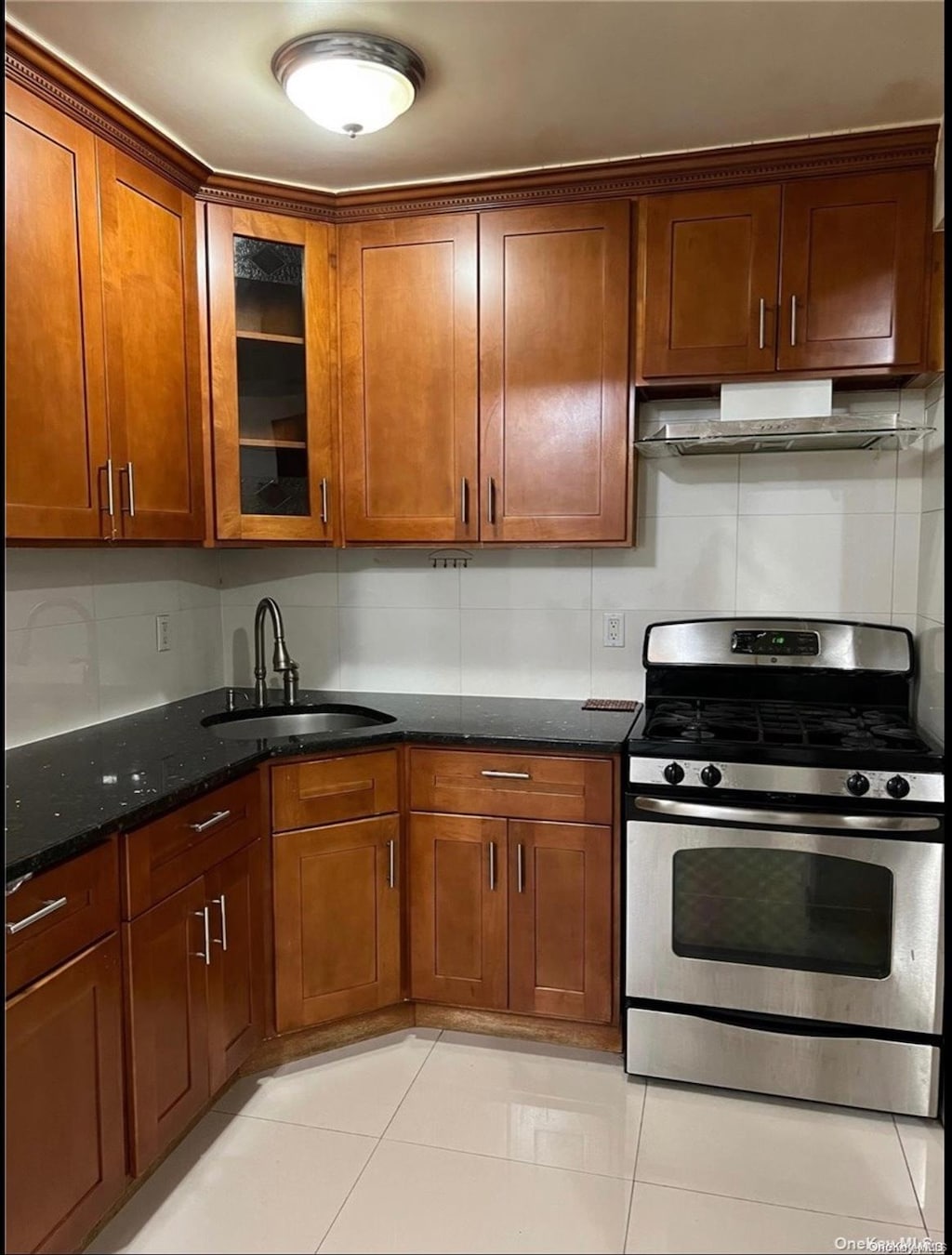 kitchen featuring backsplash, sink, gas range, dark stone countertops, and light tile patterned flooring