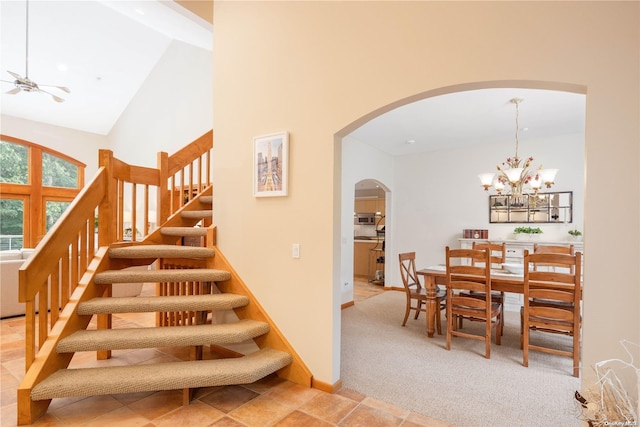 staircase with carpet, ceiling fan with notable chandelier, beam ceiling, and high vaulted ceiling