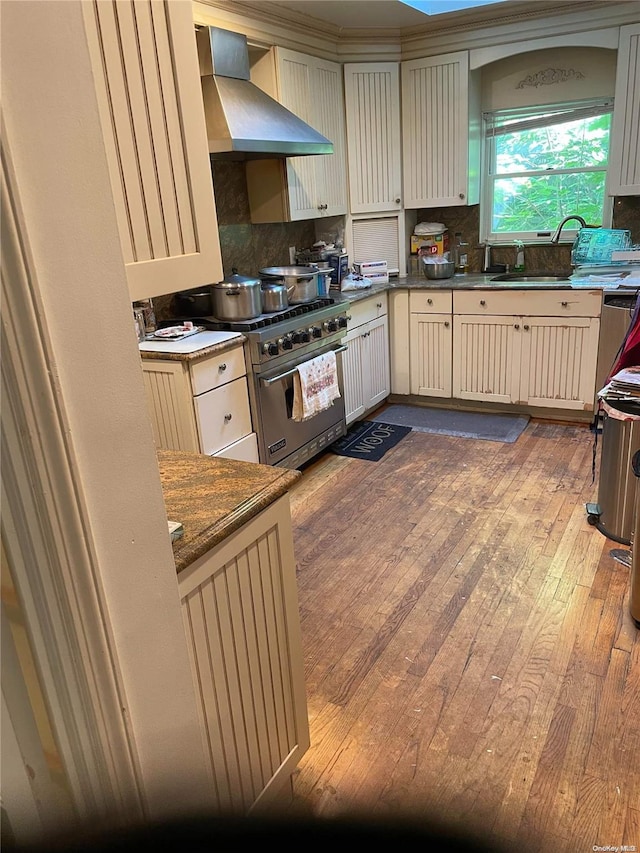 kitchen featuring tasteful backsplash, wall chimney exhaust hood, wood-type flooring, designer stove, and cream cabinetry