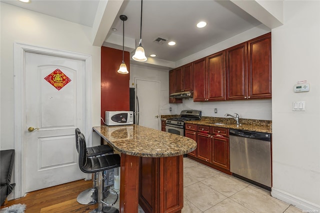 kitchen featuring dark stone counters, a kitchen breakfast bar, sink, decorative light fixtures, and stainless steel appliances