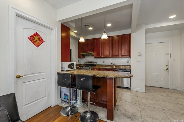 kitchen with kitchen peninsula, a kitchen breakfast bar, stainless steel appliances, decorative light fixtures, and dark stone countertops