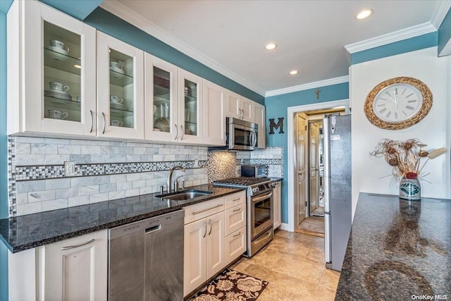 kitchen with appliances with stainless steel finishes, dark stone counters, ornamental molding, sink, and white cabinets