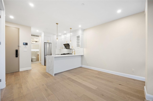 kitchen featuring pendant lighting, stainless steel fridge, white cabinets, light hardwood / wood-style floors, and kitchen peninsula