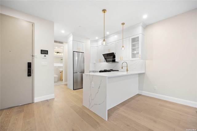 kitchen featuring stainless steel refrigerator, white cabinets, hanging light fixtures, kitchen peninsula, and light hardwood / wood-style flooring