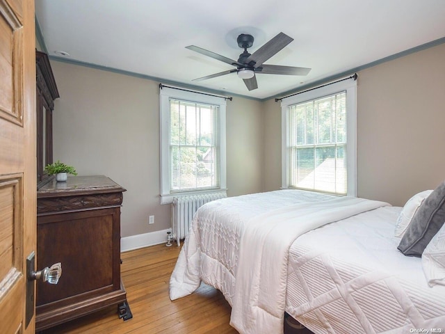 bedroom with multiple windows, light hardwood / wood-style floors, radiator, and ceiling fan