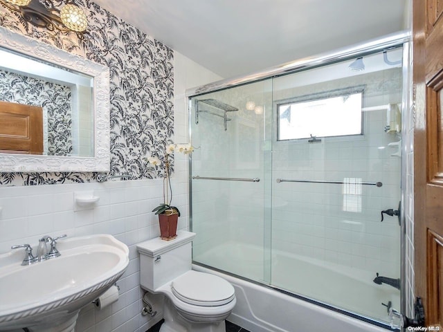 full bathroom featuring toilet, bath / shower combo with glass door, sink, and tile walls