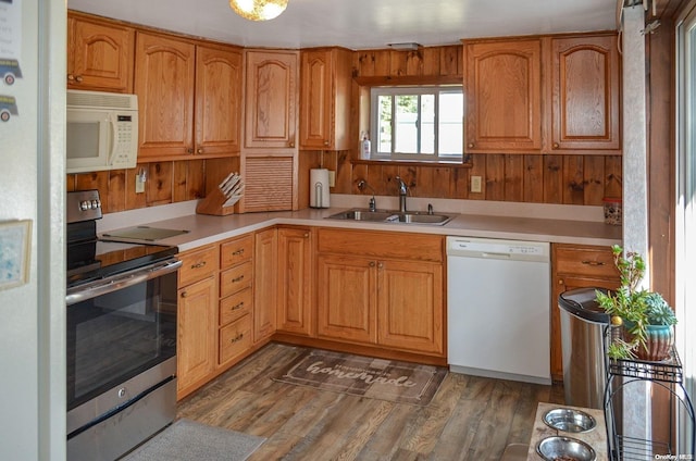 kitchen featuring wood walls, white appliances, sink, and dark wood-type flooring