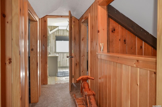 corridor with light carpet, wooden walls, and vaulted ceiling