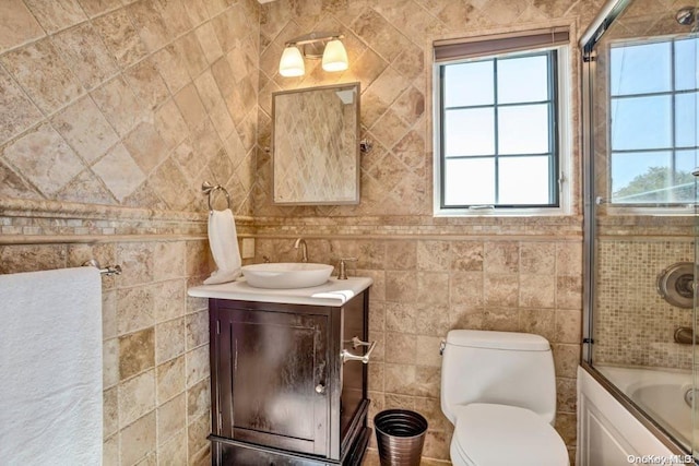 full bathroom with vanity, toilet, combined bath / shower with glass door, and tile walls