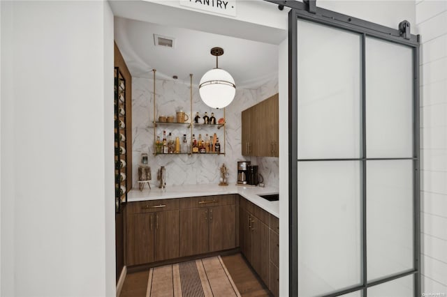 bar with pendant lighting, a barn door, tasteful backsplash, and dark hardwood / wood-style flooring