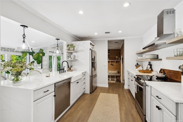 kitchen featuring wall chimney range hood, light wood-type flooring, appliances with stainless steel finishes, decorative light fixtures, and white cabinetry