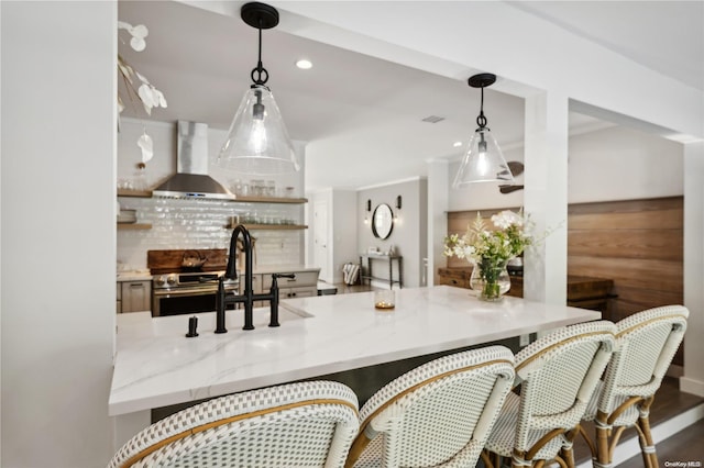 kitchen with stainless steel electric range, light stone counters, hanging light fixtures, and wall chimney range hood