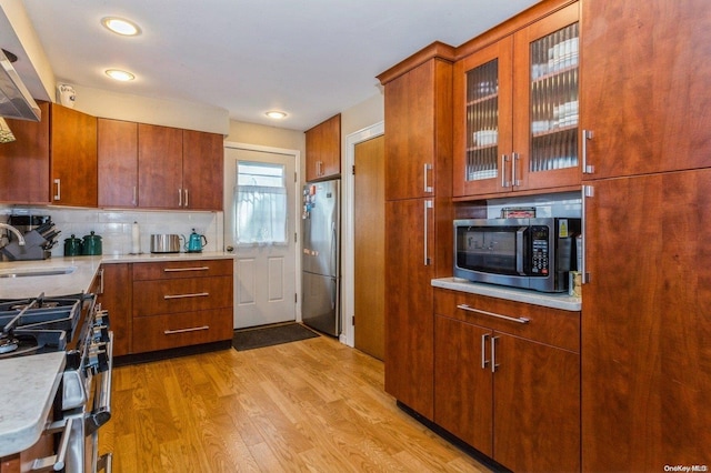 kitchen with backsplash, sink, light hardwood / wood-style flooring, and appliances with stainless steel finishes