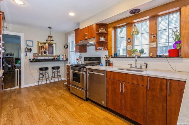 kitchen with appliances with stainless steel finishes, light wood-type flooring, decorative light fixtures, and sink