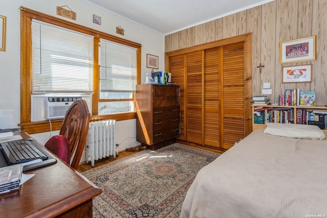 bedroom with radiator heating unit, wood-type flooring, wooden walls, a closet, and ornamental molding