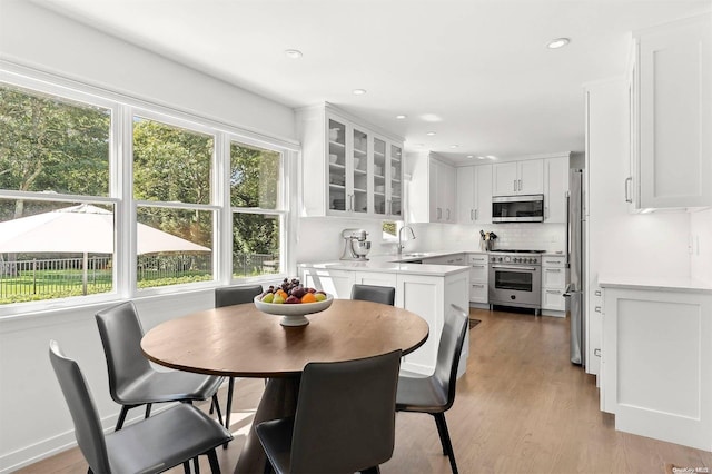 kitchen with a kitchen breakfast bar, sink, light hardwood / wood-style floors, white cabinetry, and stainless steel appliances