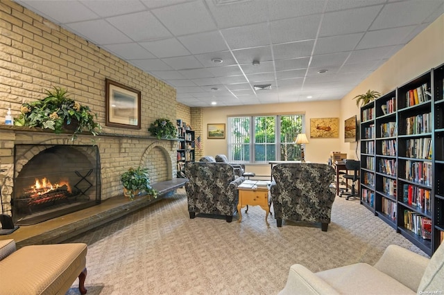 living room featuring a paneled ceiling, carpet floors, brick wall, and a brick fireplace