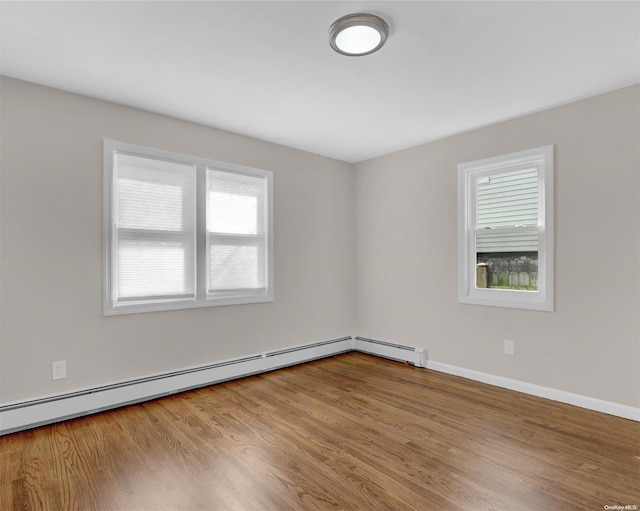 spare room featuring a baseboard heating unit, light hardwood / wood-style flooring, and a healthy amount of sunlight