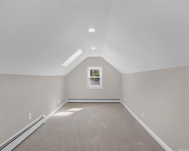 additional living space featuring vaulted ceiling with skylight, light carpet, and a baseboard heating unit