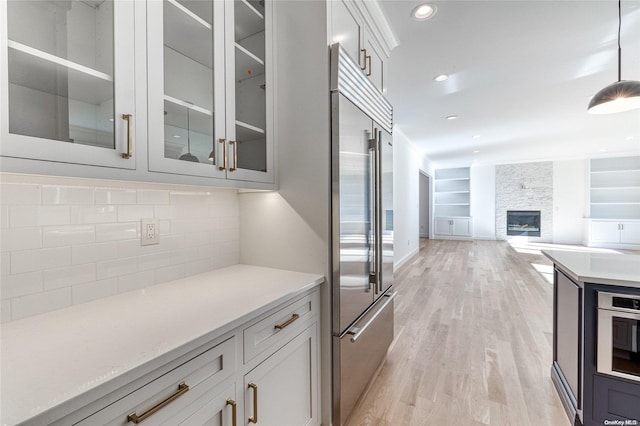 kitchen with white cabinetry, hanging light fixtures, stainless steel appliances, light hardwood / wood-style floors, and a fireplace