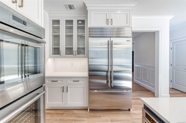 kitchen featuring stainless steel built in refrigerator, crown molding, light hardwood / wood-style floors, decorative backsplash, and white cabinets