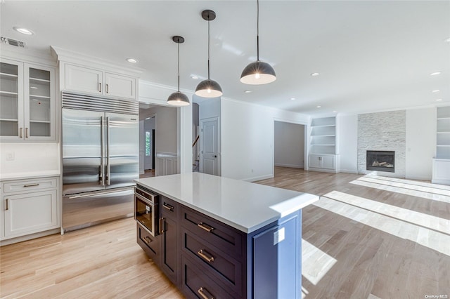 kitchen with white cabinetry, stainless steel appliances, hanging light fixtures, and light hardwood / wood-style flooring