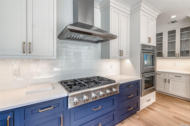 kitchen featuring white cabinetry, wall chimney exhaust hood, tasteful backsplash, light hardwood / wood-style flooring, and appliances with stainless steel finishes