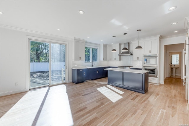 kitchen featuring pendant lighting, white cabinets, wall chimney range hood, blue cabinetry, and appliances with stainless steel finishes