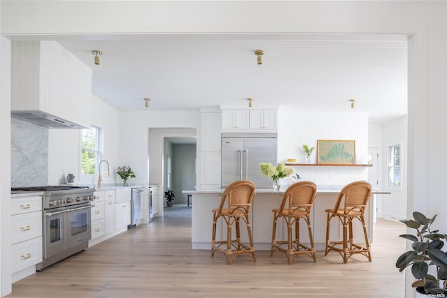 kitchen featuring white cabinets, a breakfast bar, high end appliances, and light hardwood / wood-style flooring