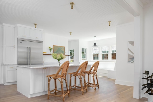 kitchen featuring built in fridge, hanging light fixtures, light wood-type flooring, a kitchen island, and white cabinetry