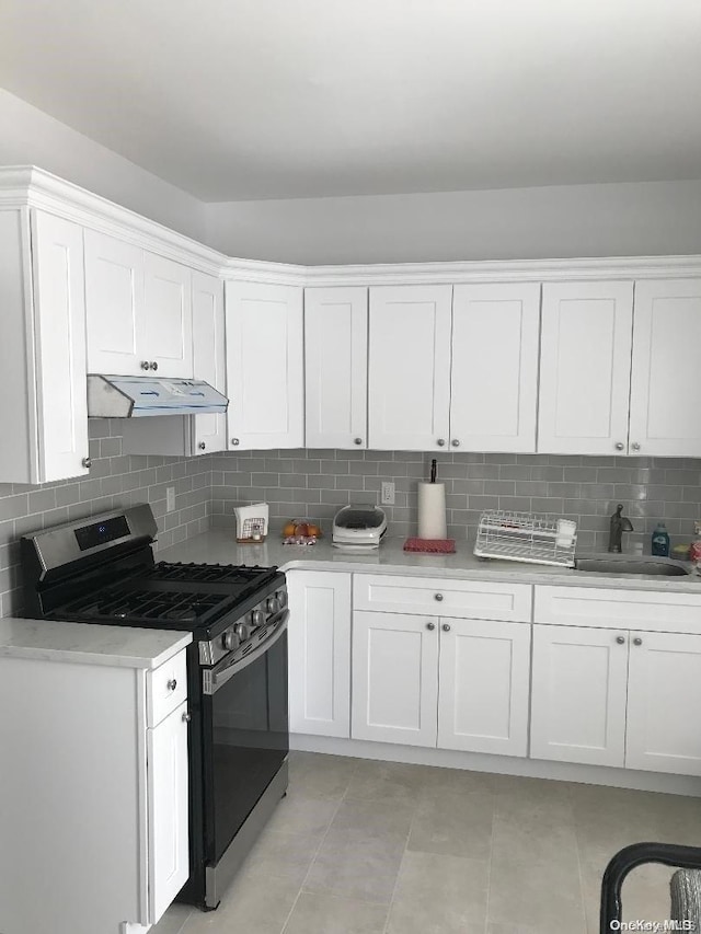 kitchen with decorative backsplash, gas stove, sink, light tile patterned floors, and white cabinets