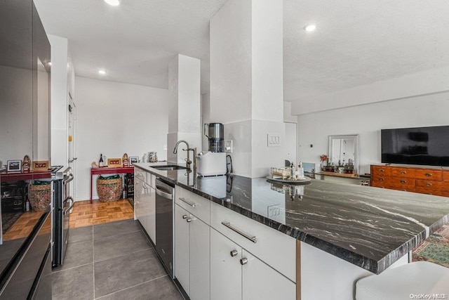 166-25 Powells Cove Blvd Unit 21G, Beechhurst, NY 11357 - kitchen featuring a sink, stainless steel dishwasher, white cabinets, dark stone counters, and a peninsula