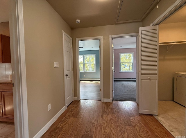 corridor with washer / dryer, baseboard heating, and light wood-type flooring