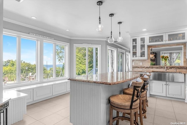 kitchen with a kitchen bar, crown molding, white cabinets, a center island, and light tile patterned flooring