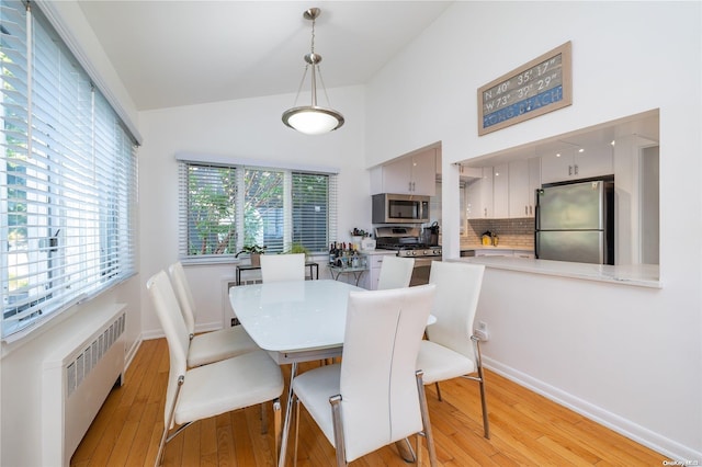 dining space with radiator heating unit, vaulted ceiling, and light hardwood / wood-style flooring