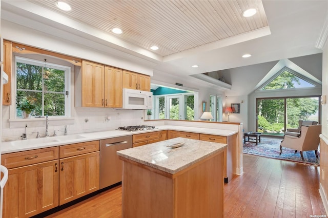 kitchen featuring sink, a center island, a raised ceiling, appliances with stainless steel finishes, and light wood-type flooring