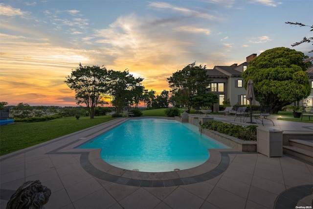 pool at dusk featuring a patio and a lawn