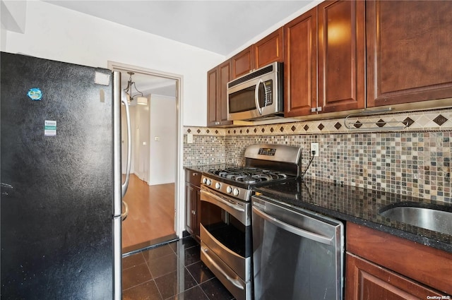 kitchen featuring decorative backsplash, appliances with stainless steel finishes, dark stone counters, dark tile patterned floors, and sink