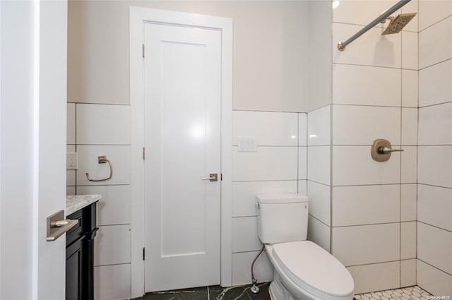 bathroom with a tile shower, vanity, tile walls, and toilet