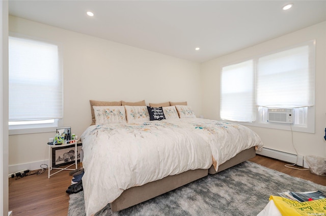 bedroom featuring hardwood / wood-style flooring, baseboard heating, and cooling unit