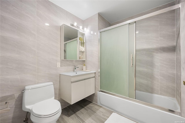 full bathroom featuring vanity, toilet, shower / bath combination with glass door, and tile walls