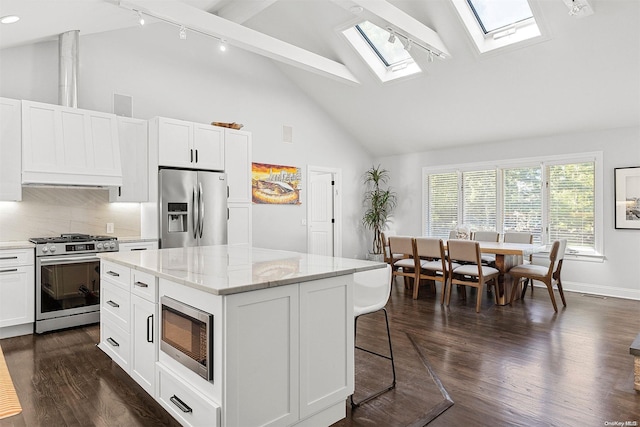 kitchen with a skylight, white cabinetry, a center island, stainless steel appliances, and high vaulted ceiling